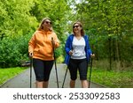 Portrait of two pretty young women dressed sporty practicing Nordic walking on background of beautiful green trees in city park on spring day. Training of Nordic walking in park. 