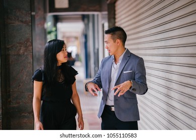 A Portrait Of Two Professional Business People Walking And Talking. They Are Deep In Conversation As They Walk On A Street In A City In Asia. The Man And Woman Are Both Professionally Dressed. 