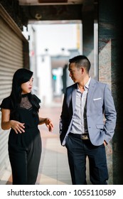 A Portrait Of Two Professional Business People Walking And Talking. They Are Deep In Conversation As They Walk On A Street In A City In Asia. The Man And Woman Are Both Professionally Dressed. 