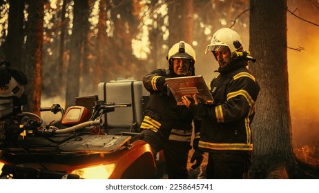 Retrato de dos bomberos profesionales parados al lado de un vehículo todo terreno, utilizando una computadora portátil de gran servicio y determinando una mejor estrategia para extinguir el incendio en tierras silvestres. Toma media.