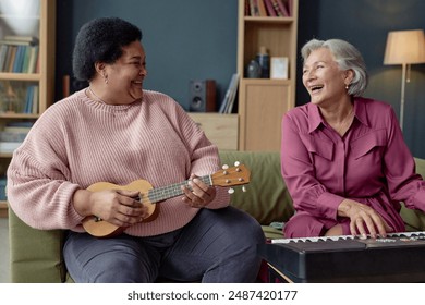 Portrait of two senior women laughing and playing music together looking at each other with piano and ukulele - Powered by Shutterstock