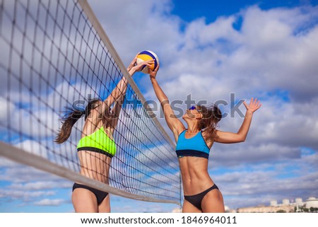 Portrait of two slim sporty girls playing beach volleyball against a bright blue sky
