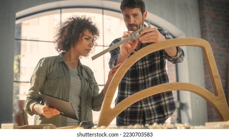 Portrait of Two Small Business Owners Using Tablet Computer and Discussing the Design of a New Wooden Chair in a Furniture Workshop. Carpenter and a Young Female Apprentice Working in Loft Studio. - Powered by Shutterstock