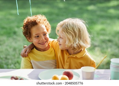 Portrait of two smiling boys embracing at picnic table outdoors while enjoying Birthday party in Summer, copy space - Powered by Shutterstock