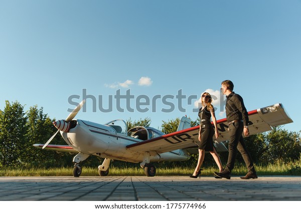 Portrait of two smiling business\
people, man and woman, walking by plane hangar in airport\
field