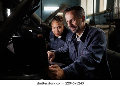 Portrait of two smiling mechanics repairing truck and using laptop in garage with accent light - Powered by Shutterstock