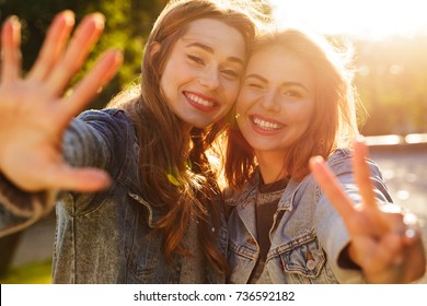Portrait of two smiling young girls waving to camera while standing outdoors
