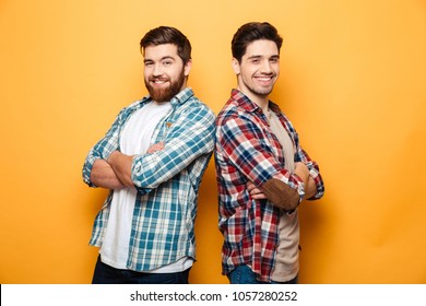 Portrait Of A Two Smiling Young Men Standing With Arms Folded Back To Back Isolated Over Yellow Background