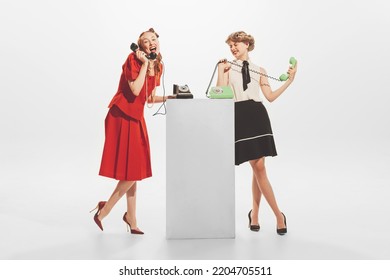 Portrait Of Two Stylish Woman In Retro Clothes Talking On Vintage Phone Isolated Over White Studio Background. Gossips, Rumors. Concept Of Retro Fashion, Style, Youth Culture, Emotions, Beauty, Ad