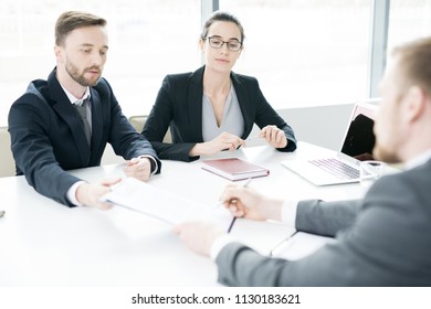 Portrait Of Two Successful Business People, Man And Woman,  Talking To Partner And Showing Him Contract Sitting Across Meeting Table In Conference Room, Copy Space