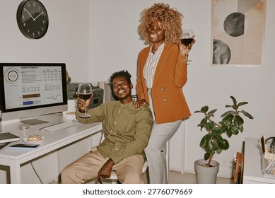 Portrait of two successful developers holding wine glasses and celebrating excellent project, they smiling widely