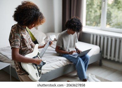 Portrait of two teenagers at home, focus on young African-American woman playing electric guitar - Powered by Shutterstock