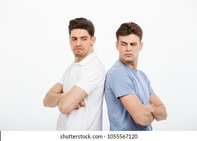 Portrait Of Two Upset Young Men Standing Back To Back With Arms Folded Isolated Over White Background