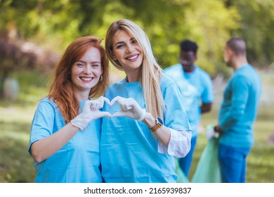 A Portrait Of Two Volunteers, Standing, Hugging, Smiling, Making A Heart With Their Hands And Looking At The Camera, After Cleaning The Public Park, Have The Same Blue T-shirts.