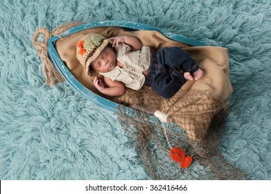 Portrait of a two week old newborn baby boy. He is sleeping in a miniature boat and wearing a fisherman's hat, vest and jeans. Shot in the studio on an aqua colored flokati rug.