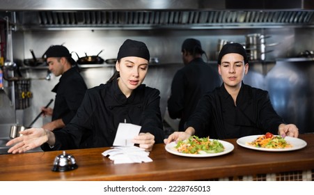 Portrait of two women chefs working in modern open kitchen, checking orders and giving out ready meals - Powered by Shutterstock