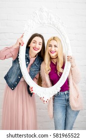 Portrait of two women friends in the frame on the white wall background