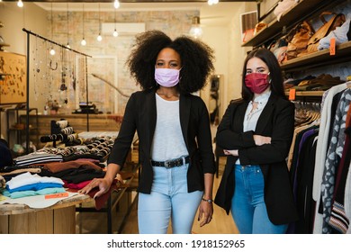 Portrait of two women owners of the clothes shop at the entrance to welcome customers during the Coronavirus Covid-19 pandemic wearing protective face masks - Millennial initiate a start-up business - Shutterstock ID 1918152965