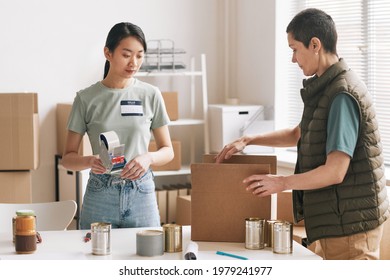 Portrait of two women packing boxes while volunteering at charity and donations event