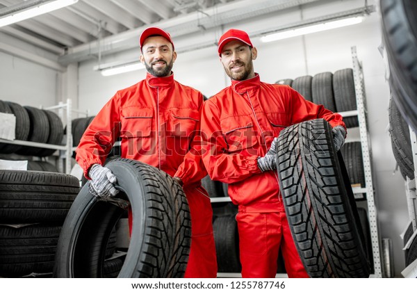 Portrait of a two workers in red uniform\
with car tires at the warehouse of the car\
service