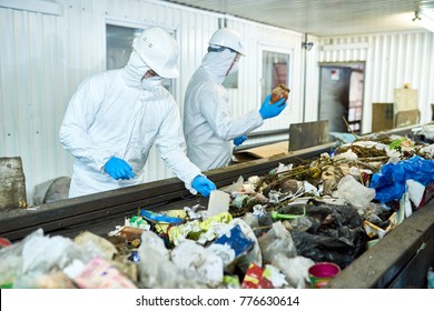 Portrait of two workers  wearing biohazard suits working at waste processing plant sorting trash on conveyor belt, copy space
