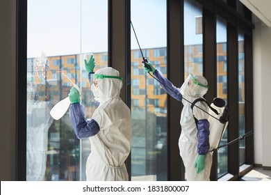 Portrait of two workers wearing hazmat suits disinfecting office windows in sunlight, copy space - Powered by Shutterstock