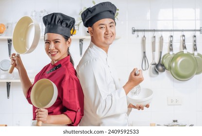 Portrait two young adult Asian professional couple chefs wearing uniform, hat, happily smiling with confidence, standing, posing, holding kitchenware in kitchen. Restaurant, Hotel, Diversity Concept - Powered by Shutterstock