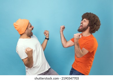 Portrait of two young adult hipster men showing yes gesture and screaming celebrating victory, success, dreams comes true, euphoria. Indoor studio shot isolated on blue background. - Shutterstock ID 2190347703