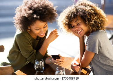 Portrait Two Young African American Women Sitting At Outdoor Cafe Looking At Cellphone