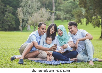 Portrait Of Two Young Asian Family In The Park Looking At Mobile Phone