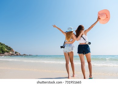 Portrait Of Two Young Asian Female Friends Walking On The Sea Shore Turn Back At Camera Laughing. Multiracial Young Women Strolling Along A Beach.