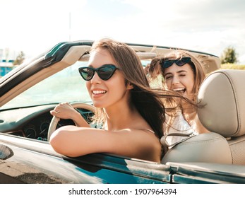 Portrait of two young beautiful and smiling hipster female in convertible car. Sexy carefree women driving cabriolet. Positive models riding and having fun in sunglasses