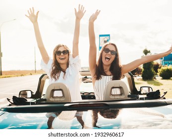 Portrait Of Two Young Beautiful And Smiling Hipster Female In Convertible Car. Sexy Carefree Women Driving Cabriolet. Positive Models Riding And Having Fun In Sunglasses. Raising Hands