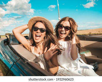 Portrait of two young beautiful and smiling hipster female in convertible car. Sexy carefree women driving cabriolet. Positive models riding and having fun in sunglasses