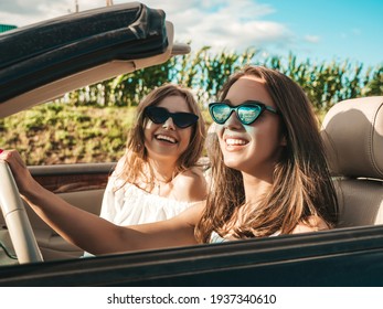 Portrait Of Two Young Beautiful And Smiling Hipster Female In Convertible Car. Sexy Carefree Women Driving Cabriolet. Positive Models Riding And Having Fun In Sunglasses Outdoors.Enjoying Summer Days