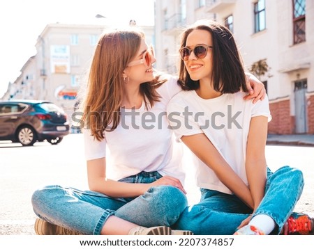 Portrait of two young beautiful smiling hipster female in trendy summer white t-shirt clothes. carefree women posing on street background. Positive models having fun, hugging and going crazy