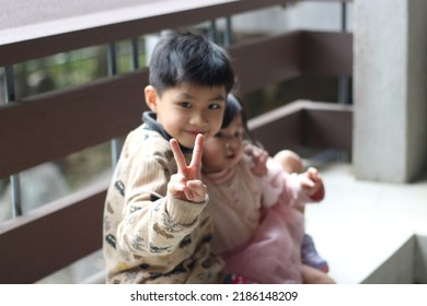 Portrait of two young children, older brother is holding younger sister and showing the V shaped gesture. Focus on the fingers - Powered by Shutterstock