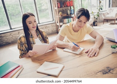 Portrait of two young college students girl reading novel book boy writing prepare exam test studying indoors in library