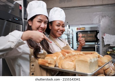 Portrait of two young female chefs in cooking uniform looking at camera with cheerful smile and proud with tray of bread in kitchen. Friend and partner of bakery foods, fresh daily bakery occupation. - Powered by Shutterstock