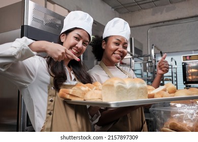 Portrait of two young female chefs in cooking uniform looking at camera with cheerful smile and proud with tray of bread in kitchen. Friend and partner of bakery foods, fresh daily bakery occupation. - Powered by Shutterstock