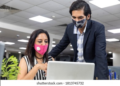 Portrait Of Two Young Indian Businesspeople Wearing Covid Protection Mask And Discussing Project At Workstation, Corporate Environment.