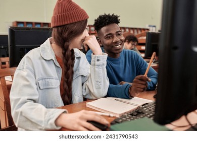 Portrait of two young students using computer in college library and pointing at screen while working on project together - Powered by Shutterstock