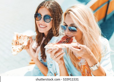 Portrait Of Two Young Women Eating Pizza Outdoors,having Fun Together.