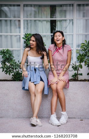 A portrait of two young women friends of different ethnicity hanging out together. One is a Chinese woman in a cheongsam and the other an Indian woman in a trendy outfit. 