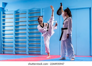 Portrait of two young women in kimono and suture, taekwondo athletes wrestling in the gym. Sportswomen demonstrating taekwondo martial art, hard training concept - Powered by Shutterstock