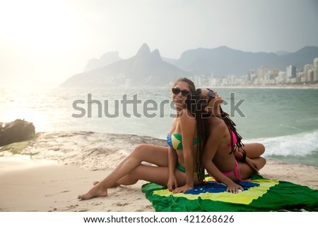 Portrait of two young women sitting on Brazilian flag, Ipanema beach, Rio De Janeiro, Brazil