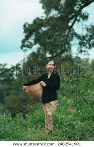 Portrait of a typical rural woman in Indonesia. Portrait of an Indonesian female farmer wearing typical Indonesian village clothes. The background is rural and outdoor rice fields.