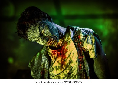 Portrait Of An Ugly Bloodied Zombie Man With Faded Eyes Illuminated By Ominous Green Light. Halloween. Horror Movie. 
