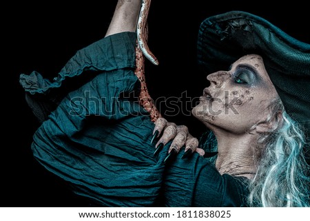 Portrait of an ugly Halloween witch talking with her poisonous snake on a black background. Scary tales. Witchcraft. 