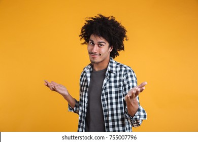 Portrait Of An Unconfident Young Afro American Man Shrugging Shoulders And Looking At Camera Isolated Over Orange Background